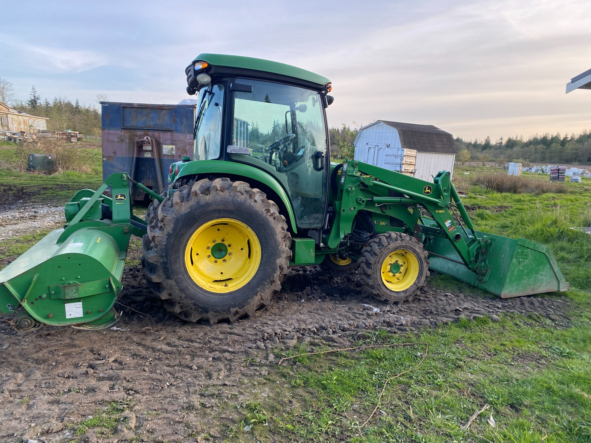 A green tractor parked on the farm with buildings and beehives in the background
